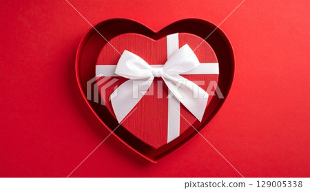 Red gift box with a ribbon and a bow on a heart-shaped design for a celebration of love, birthday, or holiday surprise Red gift box with a ribbon and a bow on a heart-shaped design for a celebration of love, birthday, or holiday surprise 129005338