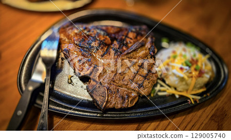 juicy grilled T bone steak, perfectly seared, served alongside a loaded baked mash potato on a warmly lit rustic dining setup. Ideal for culinary content juicy grilled T bone steak, perfectly seared, served alongside a loaded baked mash potato on a warmly lit rustic dining setup. Ideal for culinary content 129005740