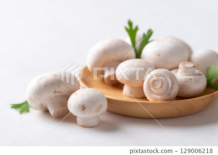 White Button mushroom or Champignon mushroom (Agaricus bisporus) on wooden plate, Food ingredient 129006218