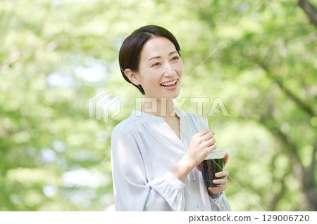 A woman in her 40s drinking iced coffee outdoors A woman in her 40s drinking iced coffee outdoors 129006720