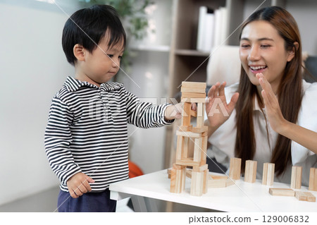 Child Development. Engaging toddler stacking wooden blocks with caregiver in a cozy indoor setting. 129006832
