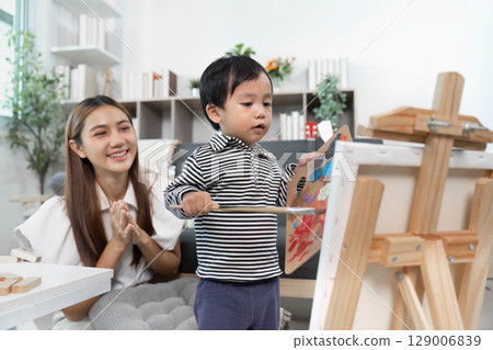Encouraging creativity. Child painting while mother watches with pride. 129006839