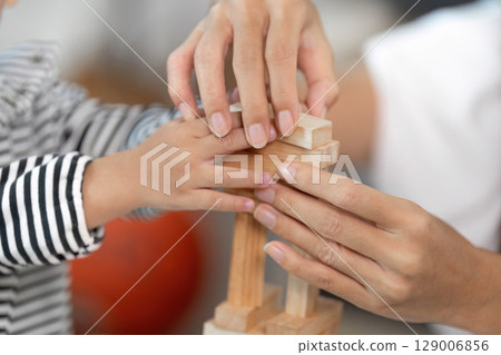 Family Bonding. Caregiver helping toddler build a wooden block tower, enhancing fine motor skills. Family Bonding. Caregiver helping toddler build a wooden block tower, enhancing fine motor skills. 129006856