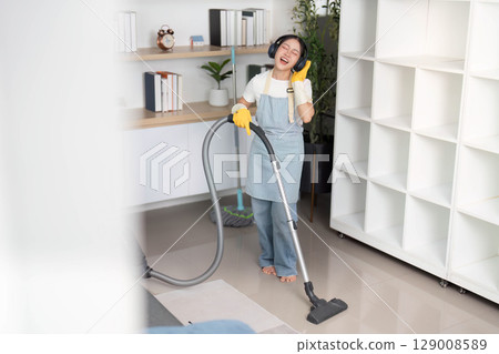 Home Cleaning. Happy woman dancing while vacuuming in a stylish living space. 129008589