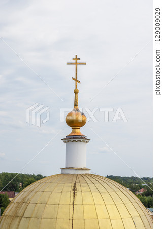 A golden church dome crowned with a cross under cloudy sky A golden church dome crowned with a cross under cloudy sky 129009029