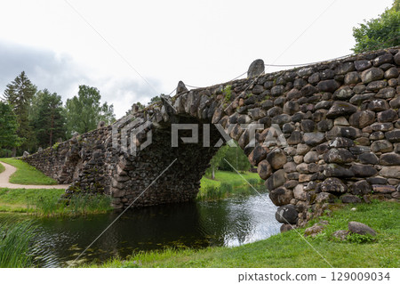 Historic Stone Arch Bridge Over Calm River in Serene Countryside Setting Historic Stone Arch Bridge Over Calm River in Serene Countryside Setting 129009034