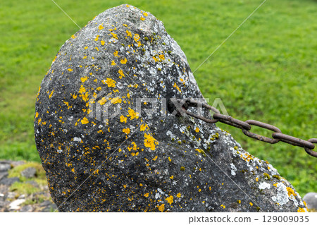 Close-Up of Weathered Stone with Metal Chain in a Green Field 129009035