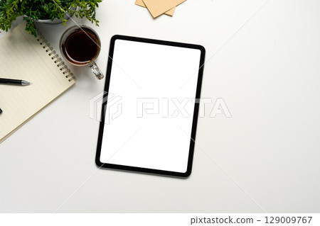 Flat lay of digital tablet mockup on white desk with coffee, notepad, and plant 129009767