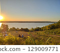 City park with a view of the Volga River and the setting sun. People relaxing in nature with a view of the sunset. Evening landscape photo, Samara region, Russia. 129009771