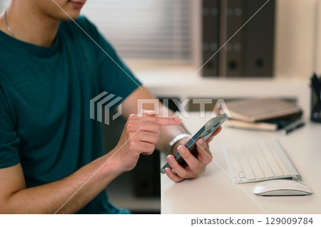 Close up of man using his smartphone in a modern workspace 129009784