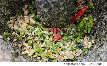 Pounding Thai Chilies and Ingredients in a Mortar and Pestle 129009840