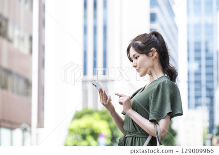 A young woman operating a smartphone in an office area 129009966