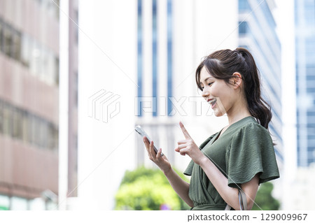 A young woman operating a smartphone in an office area 129009967