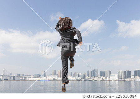 A career woman jumping through the city in a suit 129010084