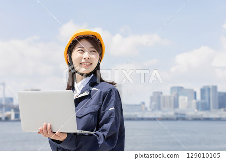 A young woman in work clothes using a laptop 129010105