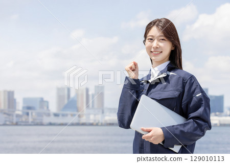 身穿工作服的年輕女子揮拳（建築、施工、土木工程、物流、工業） 129010113