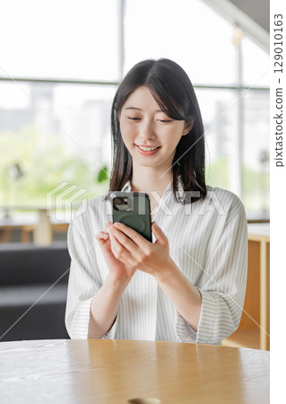A woman using a smartphone in a shared office 129010163