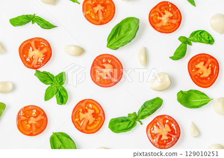 Flat lay of fresh tomato slices, garlic cloves, and basil leaves on white background 129010251