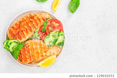Grilled chicken breast with fresh vegetables and lemon on white plate. top view. copy space Grilled chicken breast with fresh vegetables and lemon on white plate. top view. copy space 129010253