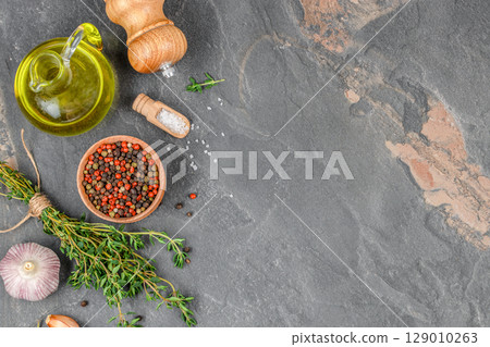 Cooking ingredients including olive oil, garlic, herbs, salt, and pepper on a dark stone kitchen surface. top view. copy space. Cooking ingredients including olive oil, garlic, herbs, salt, and pepper on a dark stone kitchen surface. top view. copy space. 129010263
