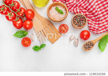 Assorted cooking ingredients with tomatoes, spices, and kitchen tools on white background with red cloth. top view. copy space. 129010299