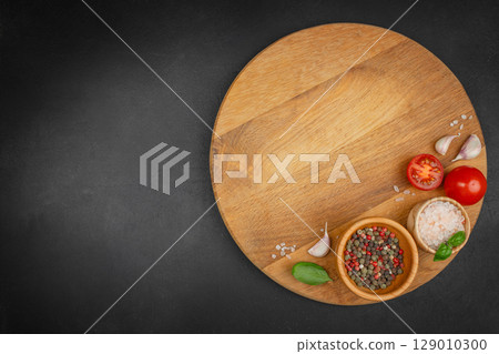 Top view of wooden round board with salt, pepper, tomatoes, garlic, and basil on black background. space for text. 129010300