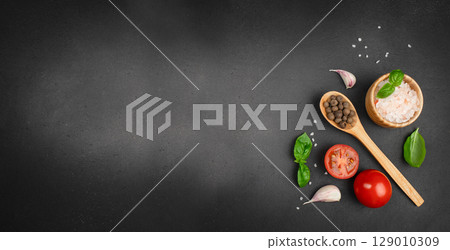 Cooking ingredients including salt, pepper, tomato, basil, and garlic on black background. Long banner format. top view. copy space. Cooking ingredients including salt, pepper, tomato, basil, and garlic on black background. Long banner format. top view. copy space. 129010309