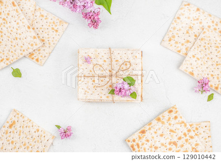 Traditional Jewish matzo crackers decorated with lilac flowers and twine for Passover celebration on white background 129010442