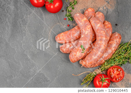 Fresh raw pork sausages with thyme and tomatoes on a dark stone background. copy space, top view. 129010445