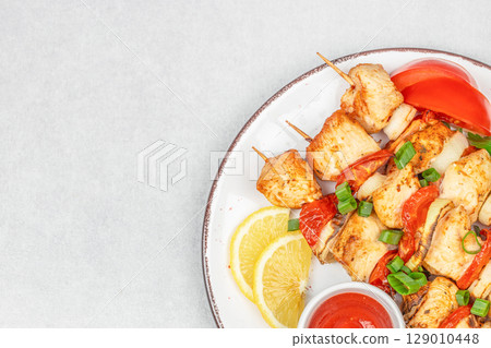 Grilled chicken skewers with vegetables, lemon slices, and dipping sauce served on a white plate. copy space, top view Grilled chicken skewers with vegetables, lemon slices, and dipping sauce served on a white plate. copy space, top view 129010448