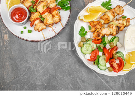 Grilled chicken skewers served with fresh salad, lemon wedges, and dipping sauces on rustic plates. copy space, top view Grilled chicken skewers served with fresh salad, lemon wedges, and dipping sauces on rustic plates. copy space, top view 129010449