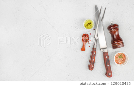 Set of kitchen knives with pepper, pink salt, olive oil, and pepper grinder on light background. copy space, top view Set of kitchen knives with pepper, pink salt, olive oil, and pepper grinder on light background. copy space, top view 129010455