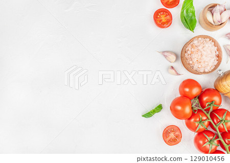 Fresh cherry tomatoes, garlic, pink salt, and basil on white background, perfect for Mediterranean cooking concepts. top view. copy space Fresh cherry tomatoes, garlic, pink salt, and basil on white background, perfect for Mediterranean cooking concepts. top view. copy space 129010456