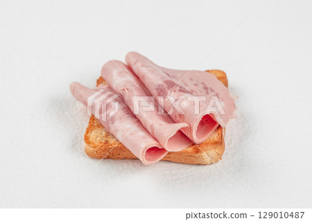 Toasted bread topped with rolled slices of luncheon meat on a white background Toasted bread topped with rolled slices of luncheon meat on a white background 129010487