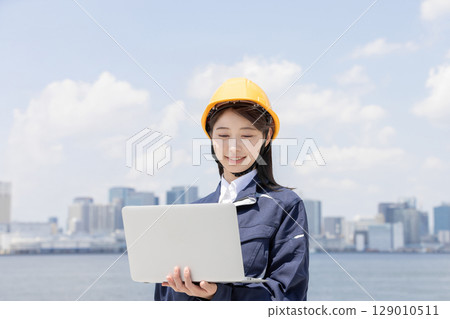 A young woman in work clothes using a laptop 129010511