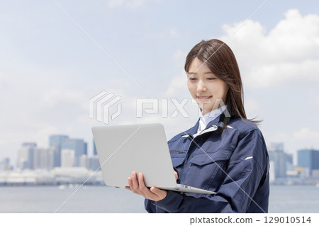 A young woman in work clothes searching on a laptop (architecture, construction, civil engineering, logistics, industry) 129010514