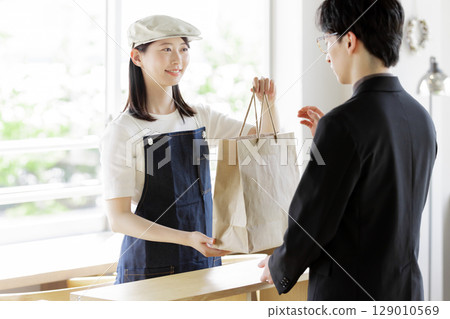 A female store clerk handing over takeout items A female store clerk handing over takeout items 129010569