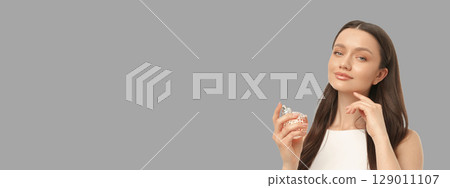 Woman in white dress holds perfume bottle confidently in studio Woman in white dress holds perfume bottle confidently in studio 129011107