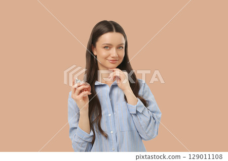 Smiling woman showcases fragrance while posing in a relaxed manner 129011108