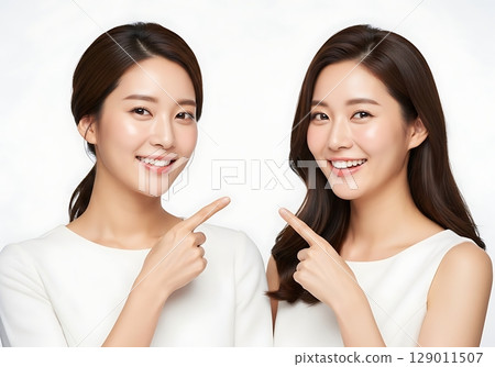 Two Radiant Asian Women with Perfect Smiles Pointing Inward on White. Two Radiant Asian Women with Perfect Smiles Pointing Inward on White. 129011507