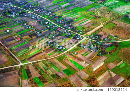 Aerial view of rural landscape with patchwork agricultural fields, tiny houses, and winding dirt road 129012224