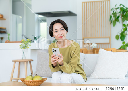 Middle-aged woman using a smartphone in the living room Middle-aged woman using a smartphone in the living room 129013261