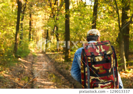 A lone man with a backpack is captured in a blurred background shot, hiking through a vibrant forest. This image evokes the spirit of summer or autumn travel and adventure 129013337