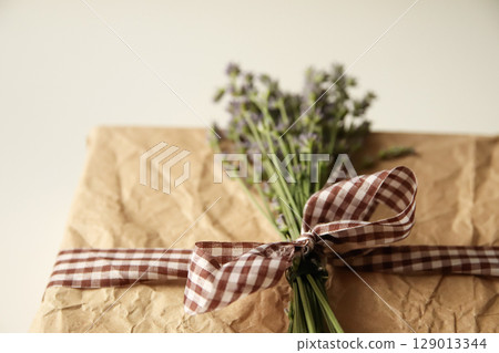 gift box wrapped with a delicate ribbon and adorned with fresh flowers, including fragrant lavender. The elegant brown and checkered background makes it perfect for a wedding or special present craft 129013344