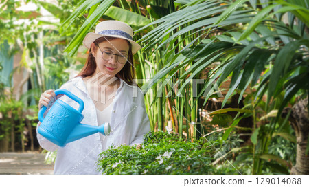 Asian woman watering tree plants with watering can in spring garden, enjoying outdoor summer activity. gardener taking care of flowering plants. gardening, outdoors, horticulture, lifestyle concept Asian woman watering tree plants with watering can in spring garden, enjoying outdoor summer activity. gardener taking care of flowering plants. gardening, outdoors, horticulture, lifestyle concept 129014088