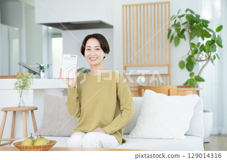 Middle-aged woman holding a calculator in the living room 129014316