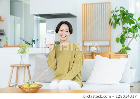 Middle-aged woman holding a calculator in the living room 129014317