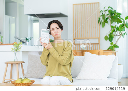 客廳裡拿著計算器的中年婦女 客廳裡拿著計算器的中年婦女 129014319