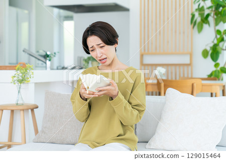 Middle-aged woman looking at her wallet in the living room Middle-aged woman looking at her wallet in the living room 129015464
