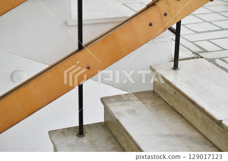 A flight of stairs with marble steps. Whitewashed walls and wooden staircase railings. The staircase of an old building. A flight of stairs with marble steps. Whitewashed walls and wooden staircase railings. The staircase of an old building. 129017123